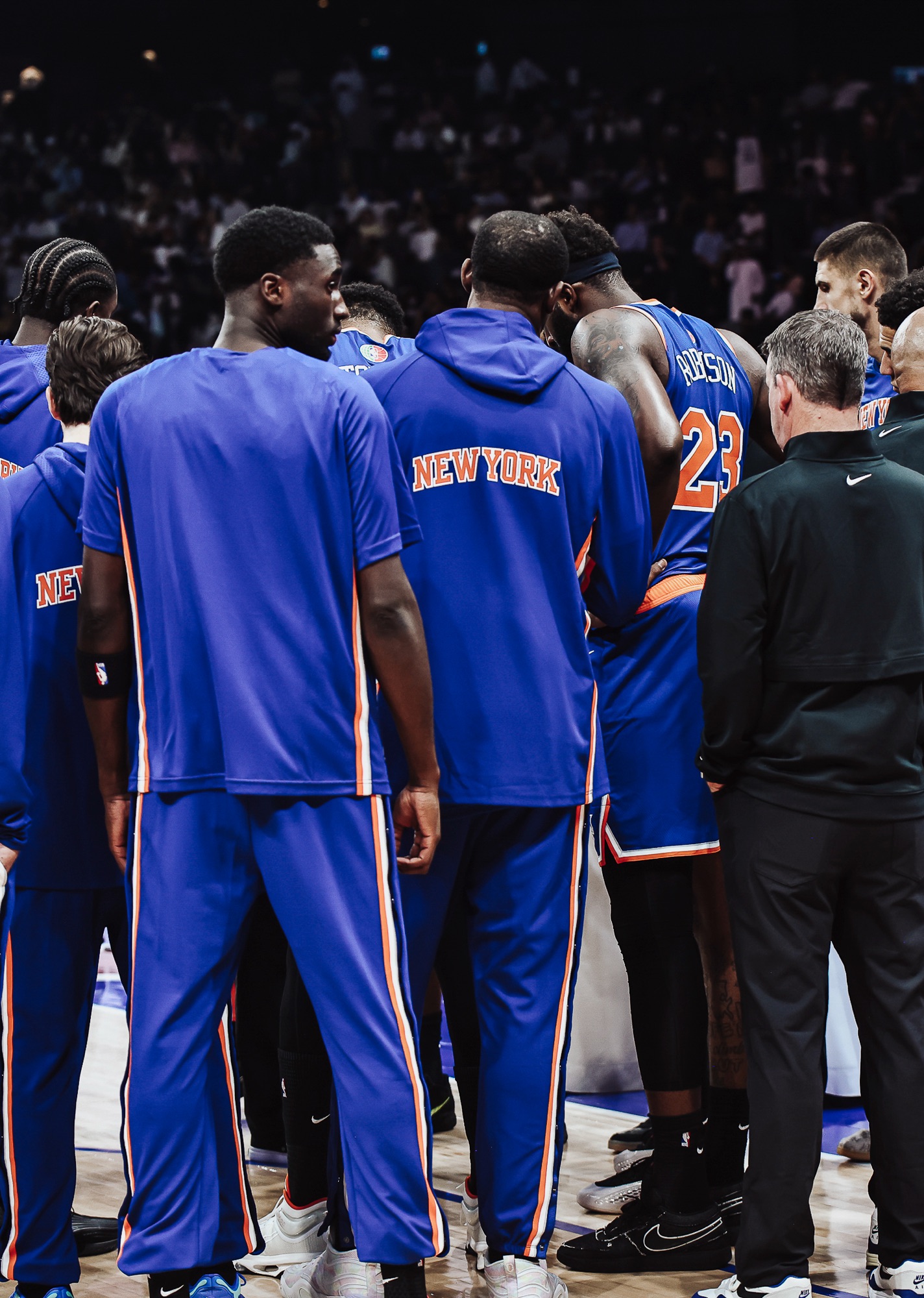 New York team in blue warm-up tops huddled on court with coaches before a game