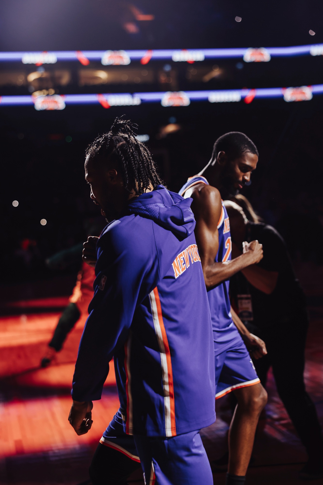 Players in New York warm-ups walking onto a dimly lit arena court