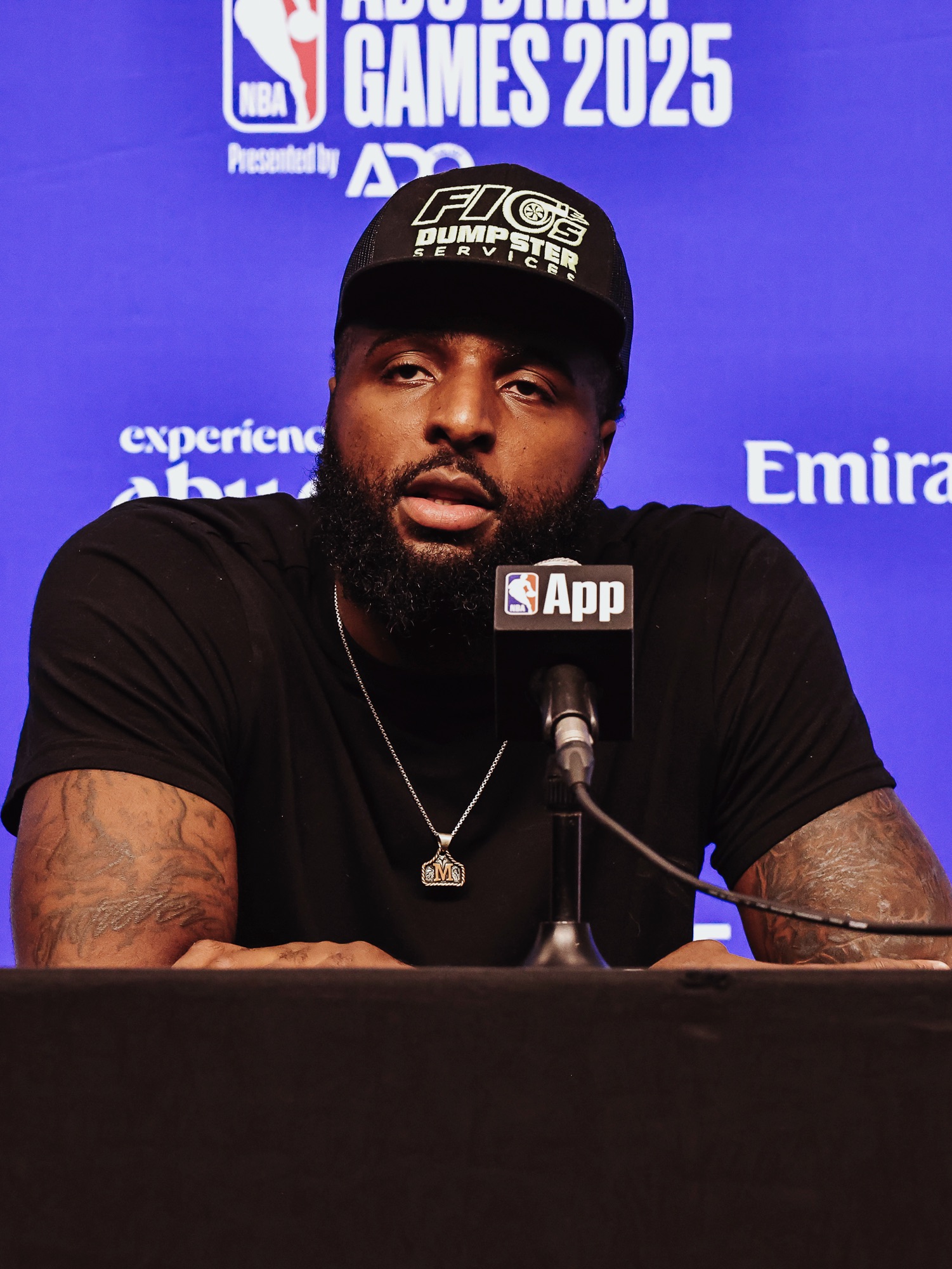 Man in a black cap and T-shirt speaking at a post-game press conference