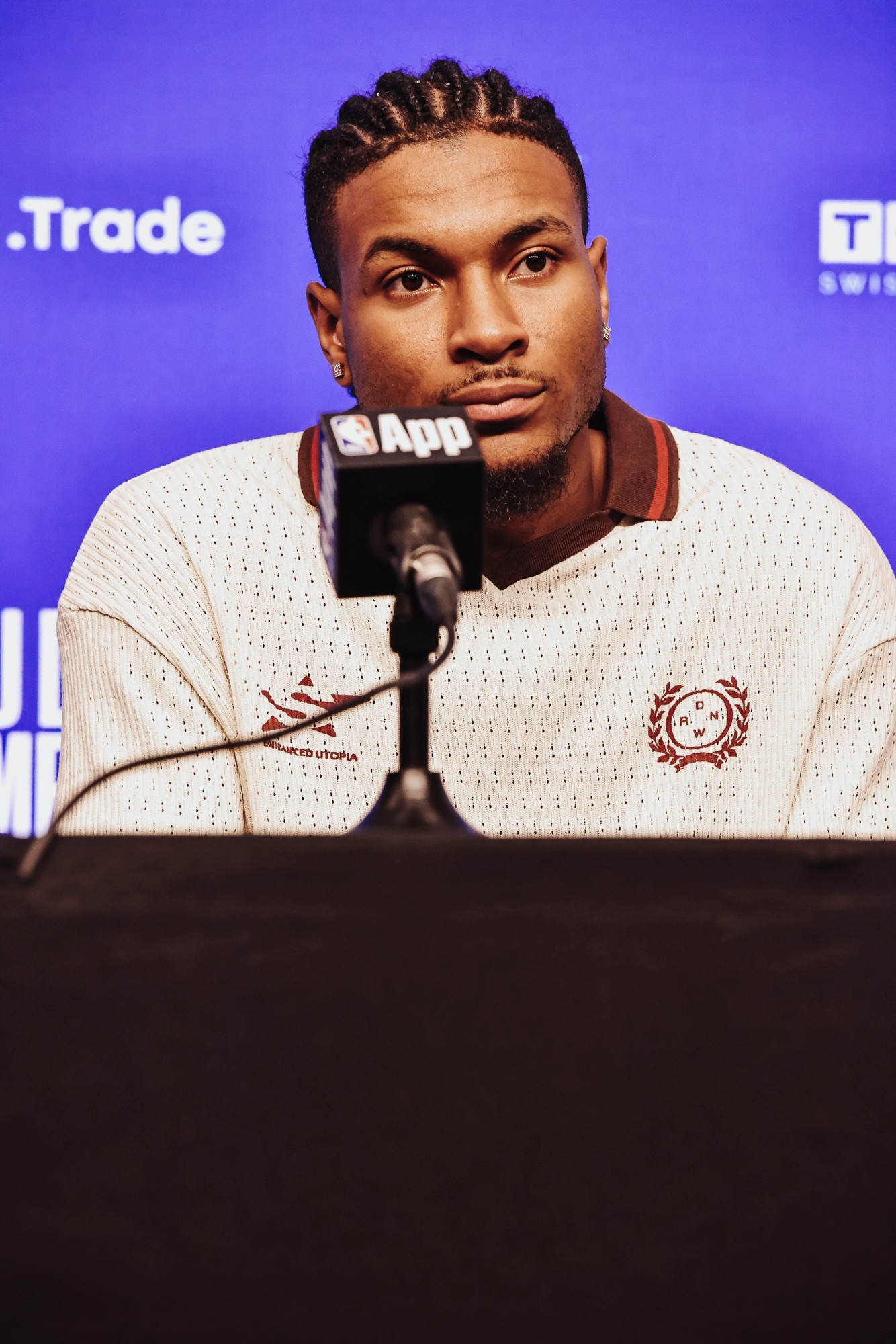 Player in a cream knit polo listening at a press conference microphone