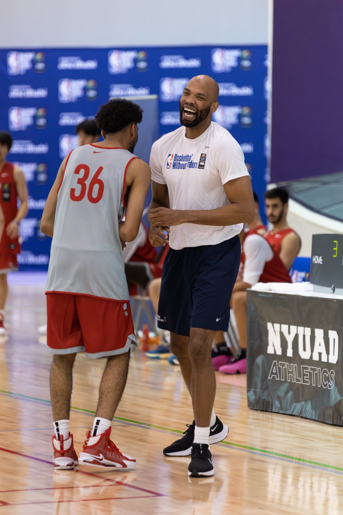 Smiling coach in a Basketball Without Borders T-shirt chatting with a young player in No. 36