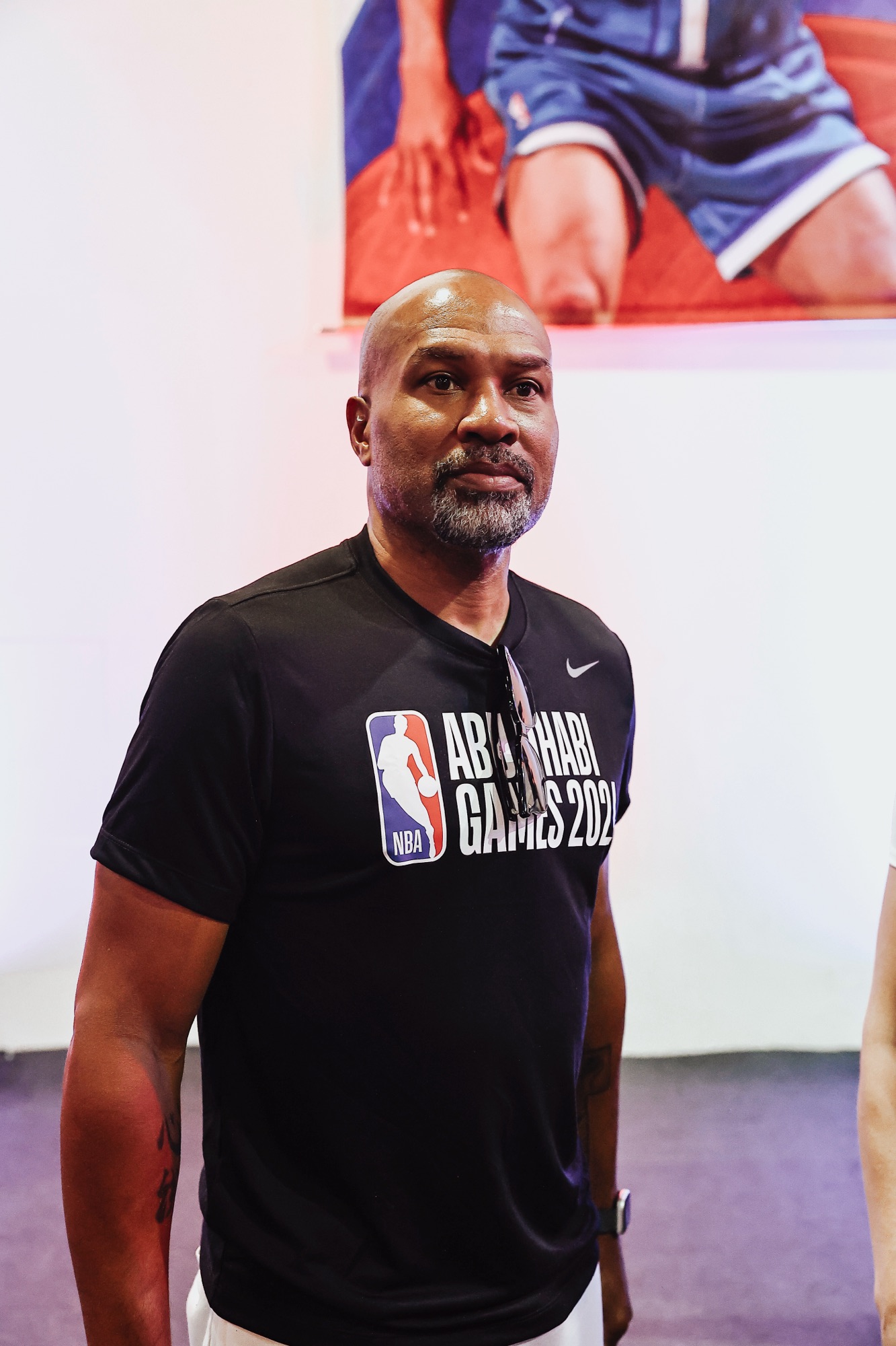 Man in a black Abu Dhabi Games T-shirt standing in front of a basketball mural