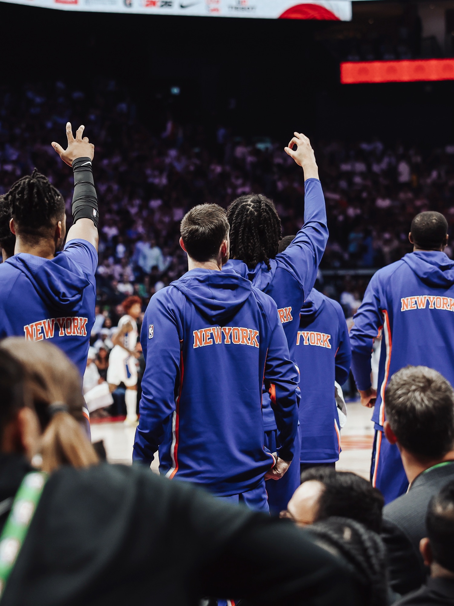 New York players in blue warm-ups raising three fingers toward the crowd from the bench
