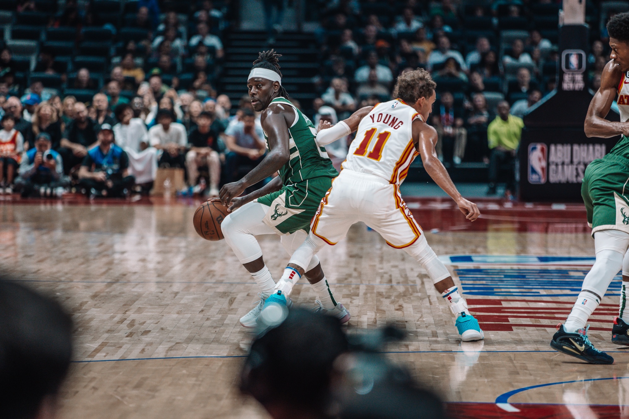 Player in a green Milwaukee jersey dribbling around an Atlanta defender in No. 11