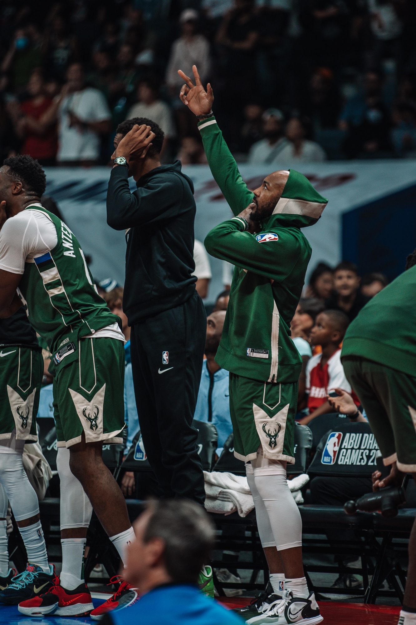 Milwaukee player in a green hoodie throwing up three fingers from the bench