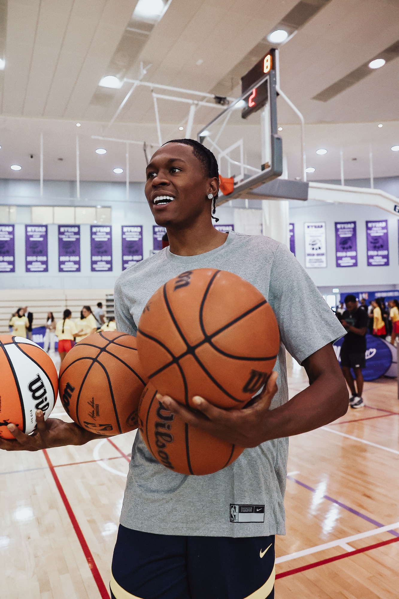 Smiling young player holding several Wilson basketballs in a bright training gym