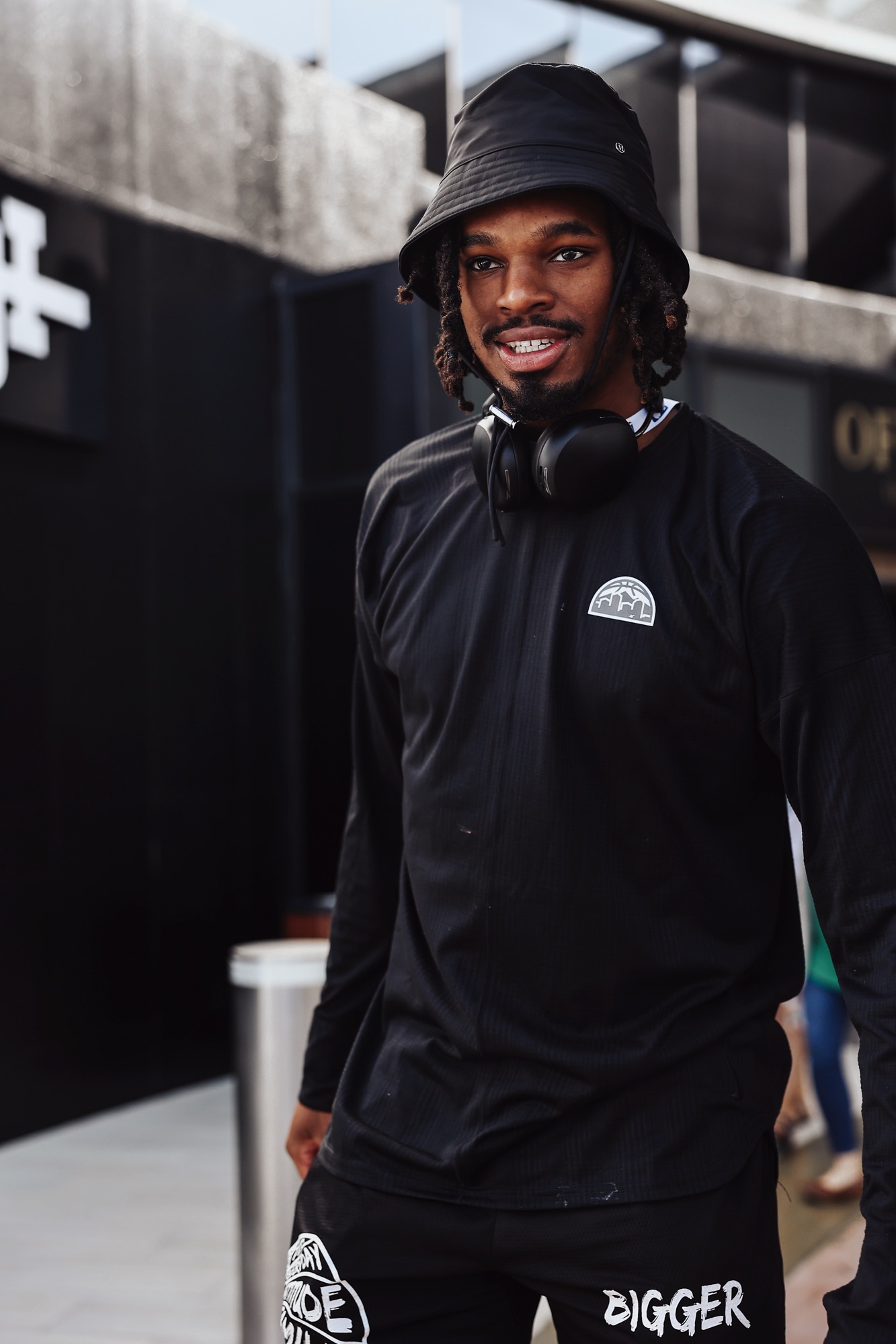 Smiling man in a black bucket hat and headphones outside an arena