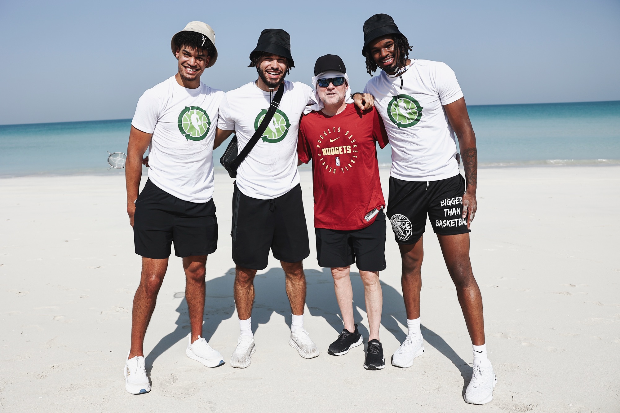 Four men in team T-shirts posing together on a white sand beach