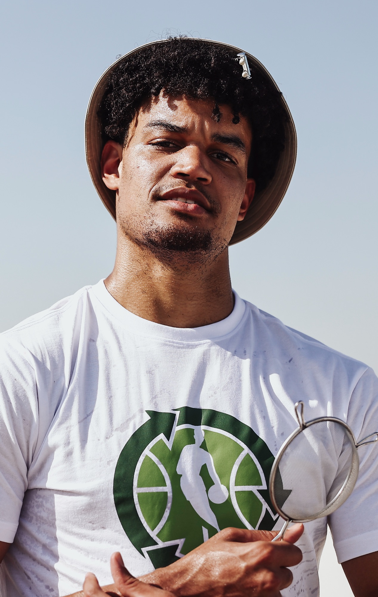 Man in a bucket hat holding a sieve during a beach clean-up, close-up