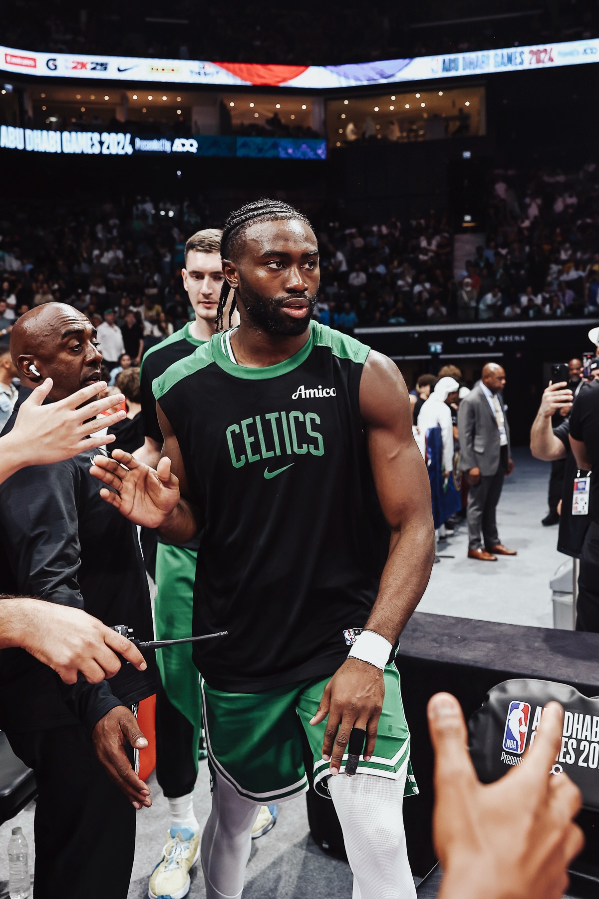 Player in a black Celtics warm-up top walking off court past reaching fans