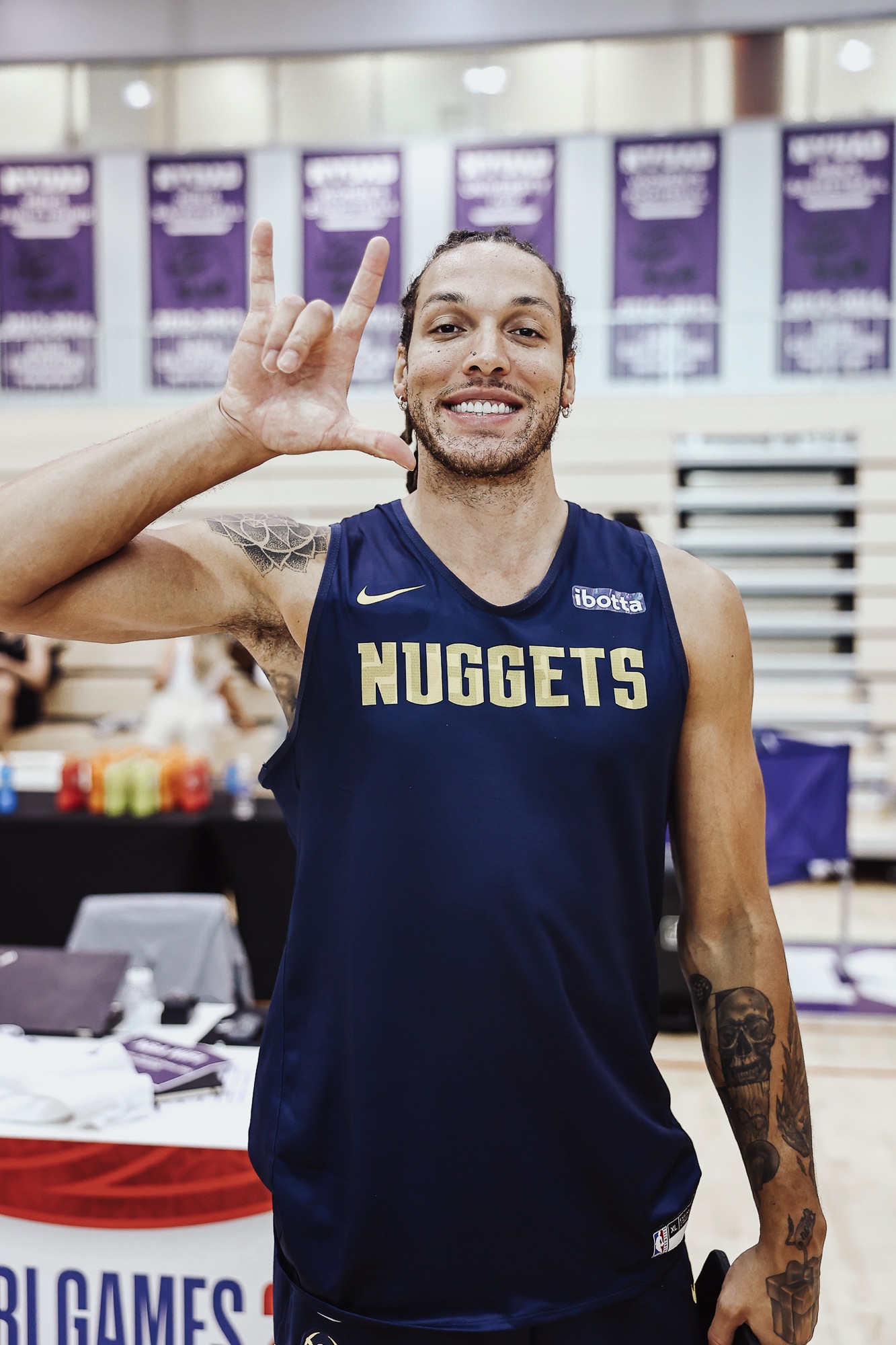 Smiling player in a navy Nuggets jersey throwing a hand sign in a training gym