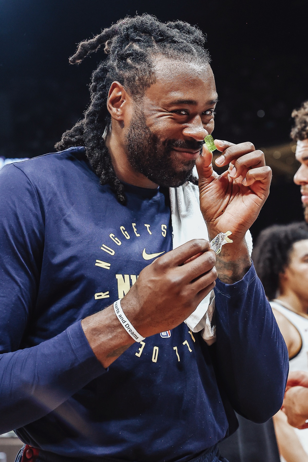 Smiling player in a navy Nuggets warm-up shirt holding a gummy sweet
