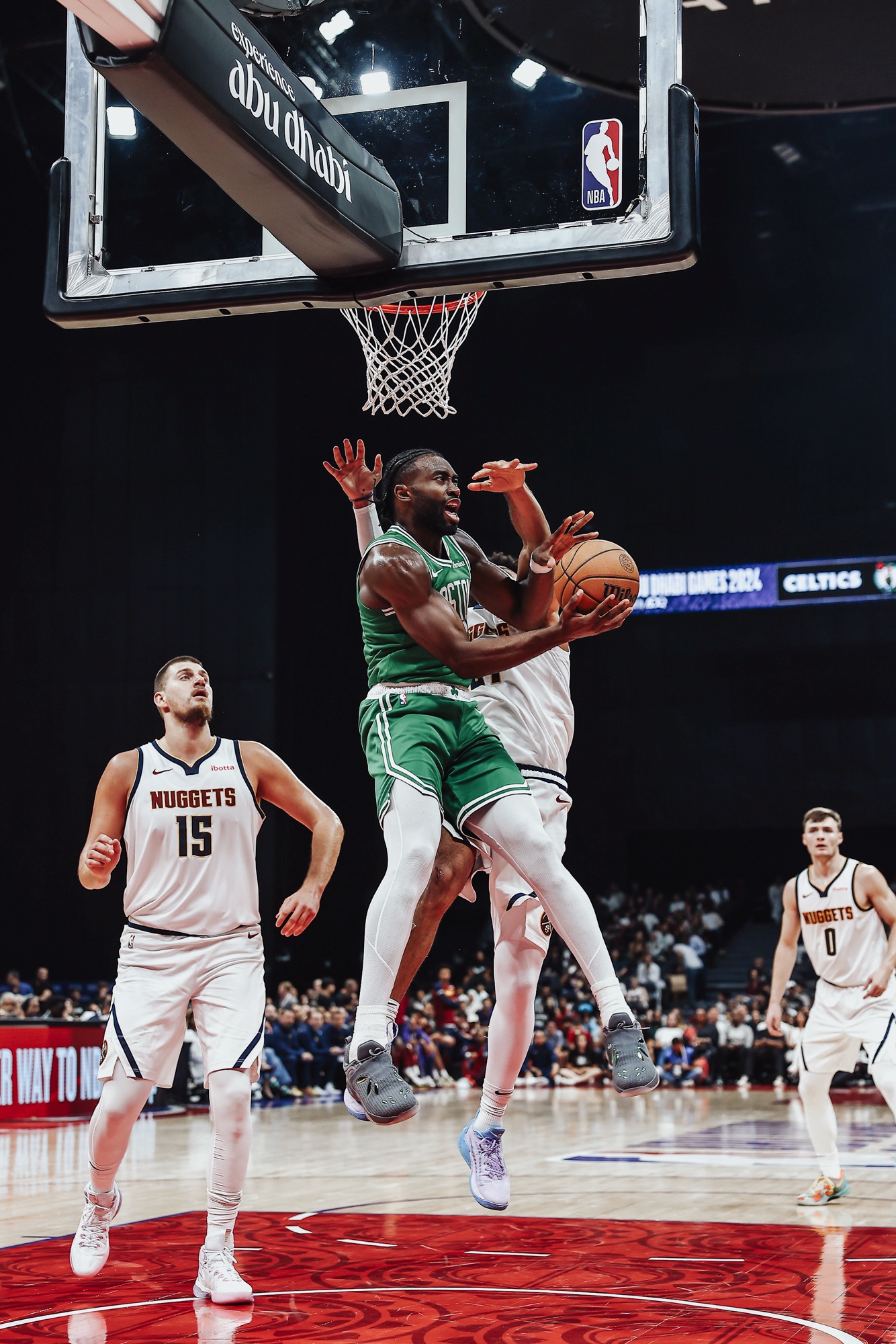 Player in a green Celtics jersey driving to the basket between Nuggets defenders