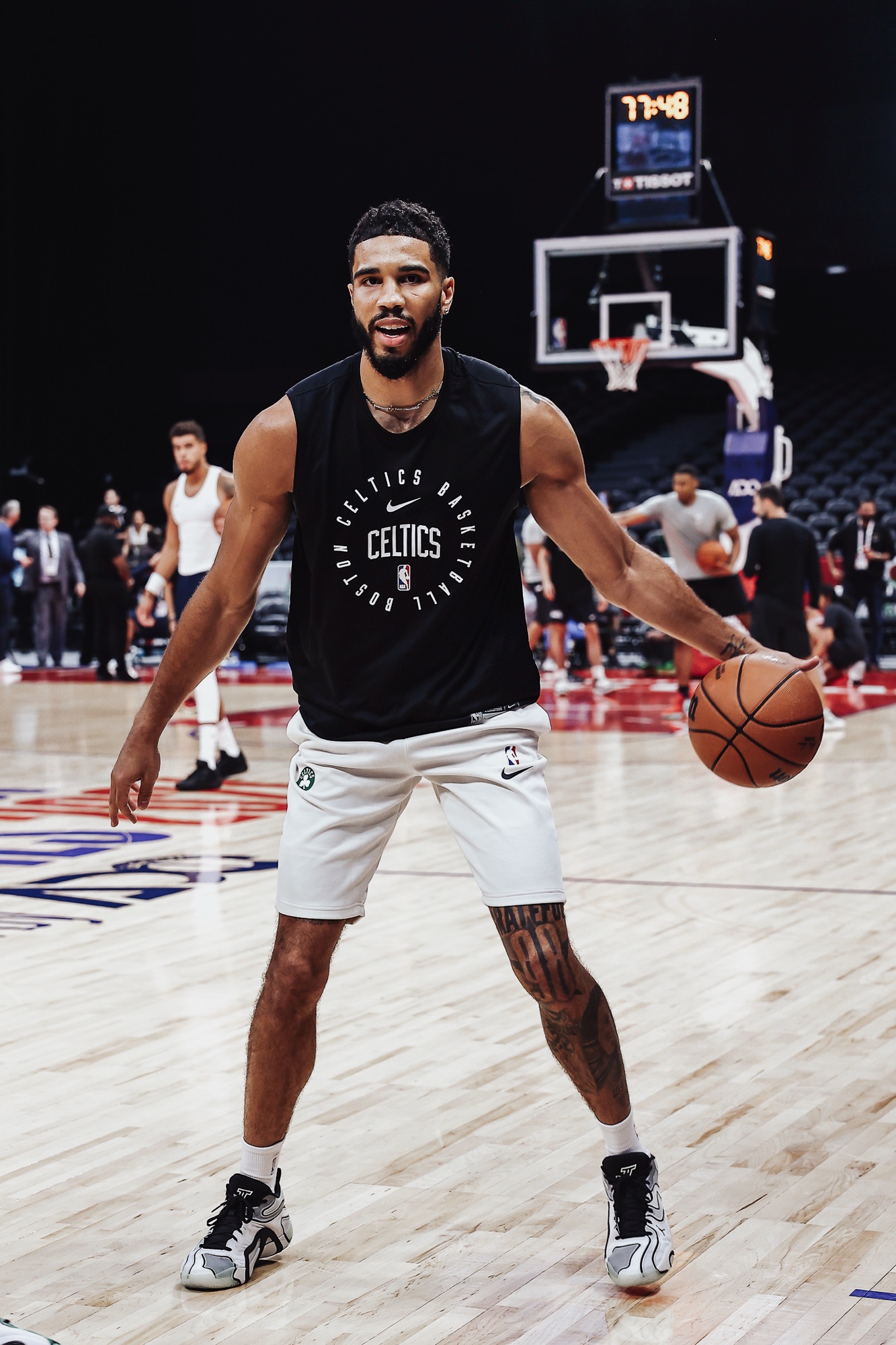 Player in a Celtics warm-up top handling the ball on court, full-length view