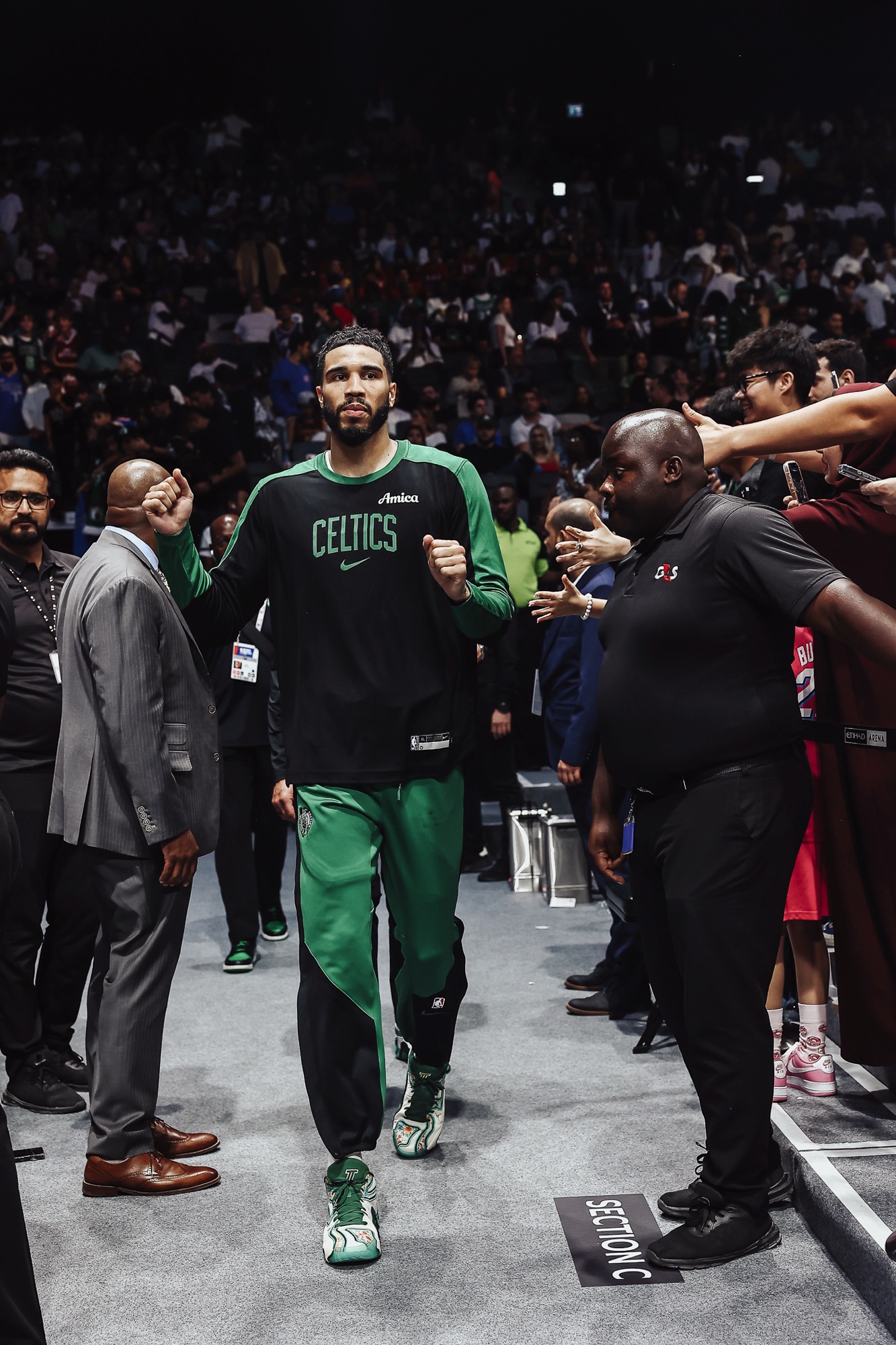Player in a Celtics shirt walking out through a tunnel of cheering fans