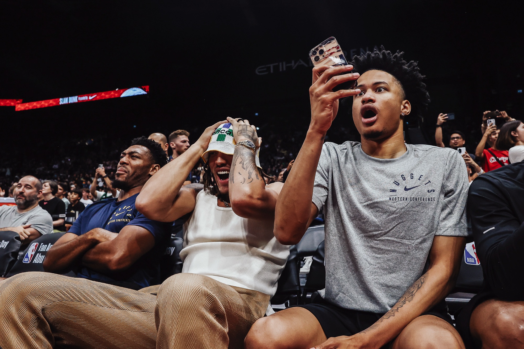 Courtside fans reacting in disbelief, one in a Nuggets T-shirt filming on his phone
