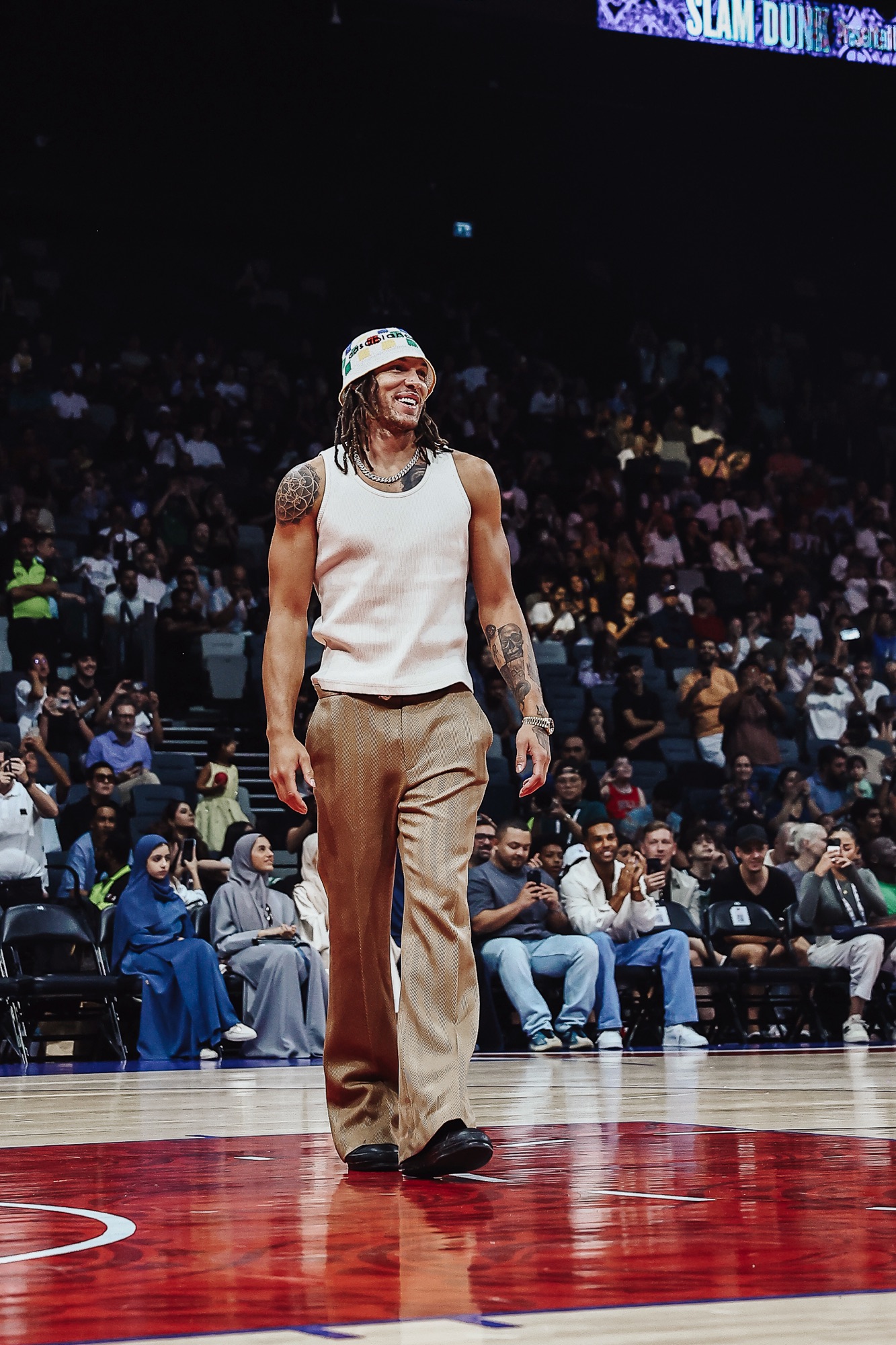 Smiling man in a bucket hat and tan trousers walking across the court before a crowd