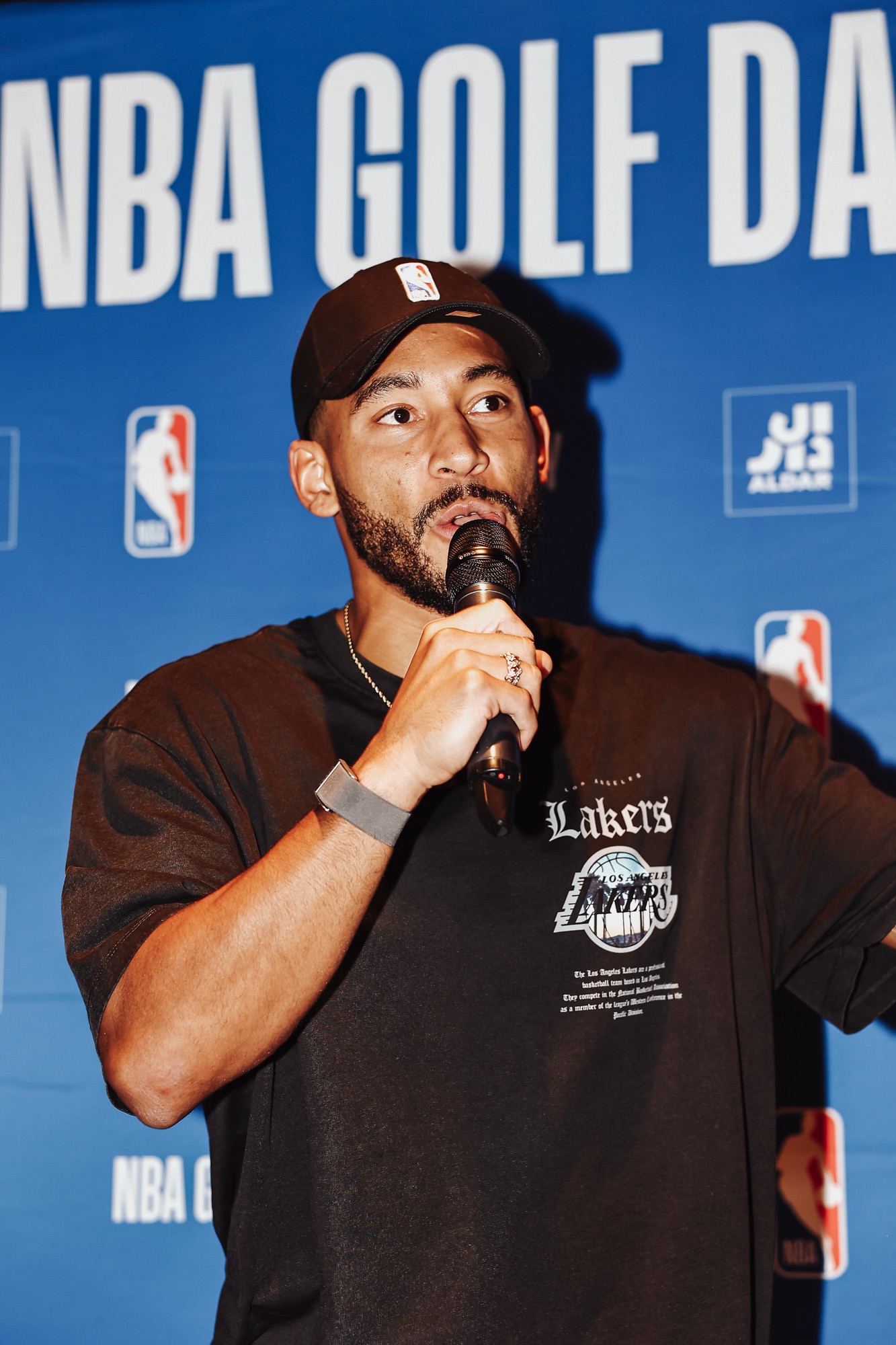 Speaker in an NBA cap and Lakers T-shirt addressing guests, close-up