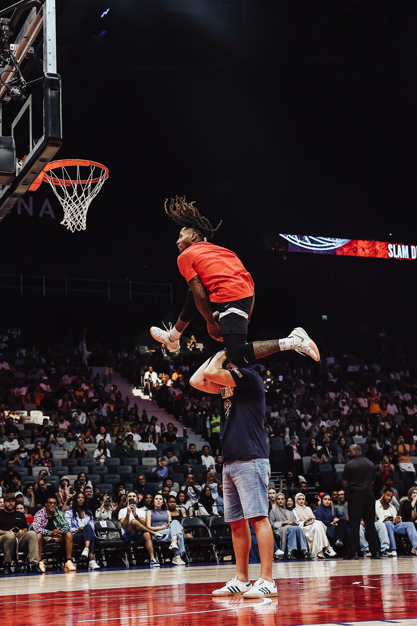 Dunker in orange leaping over a standing man during a slam dunk show