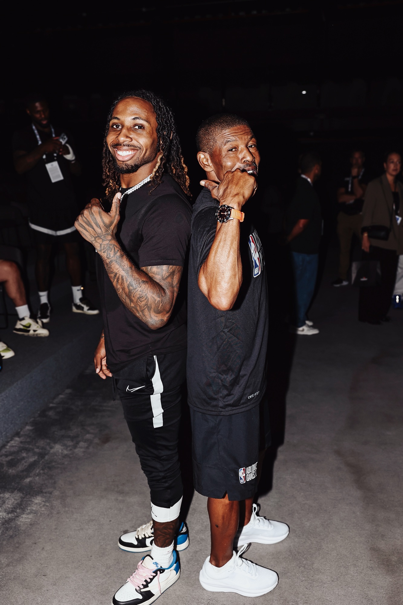 Two men in black posing back to back with playful hand gestures