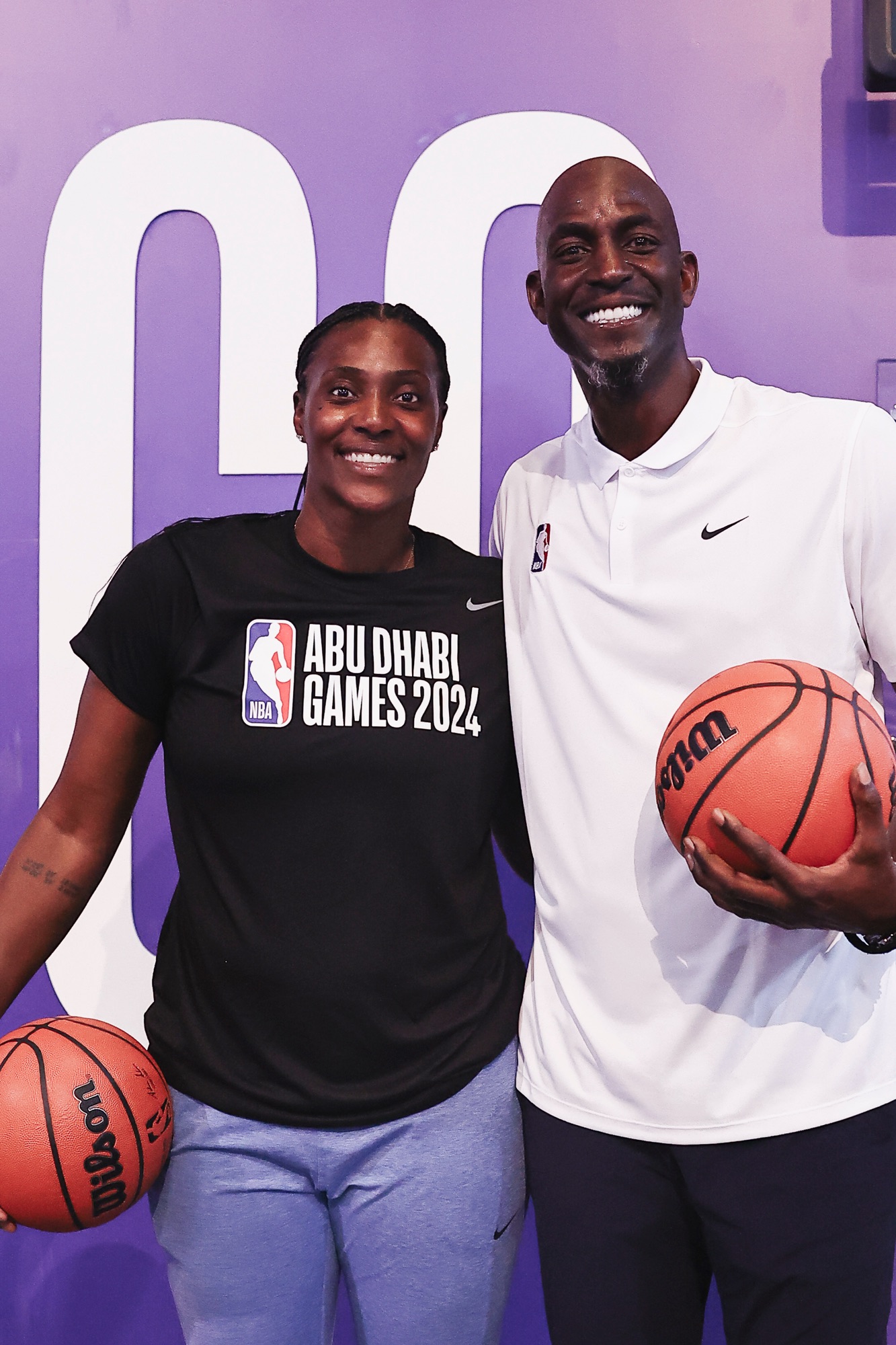 Woman in an Abu Dhabi Games 2024 shirt and man in a white polo holding basketballs