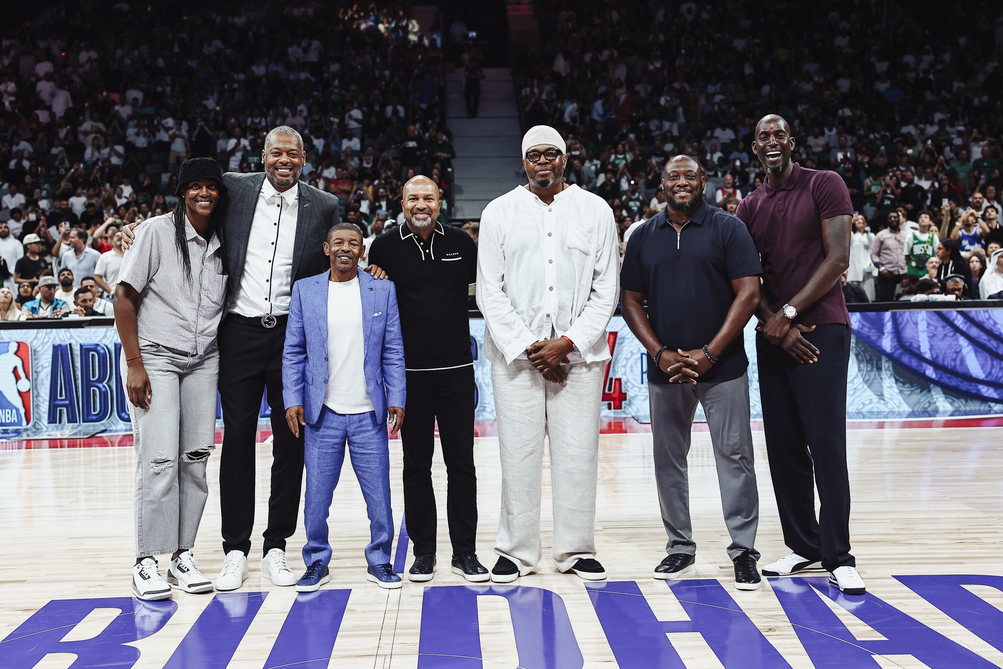 Seven guests posing together at centre court in front of a packed arena