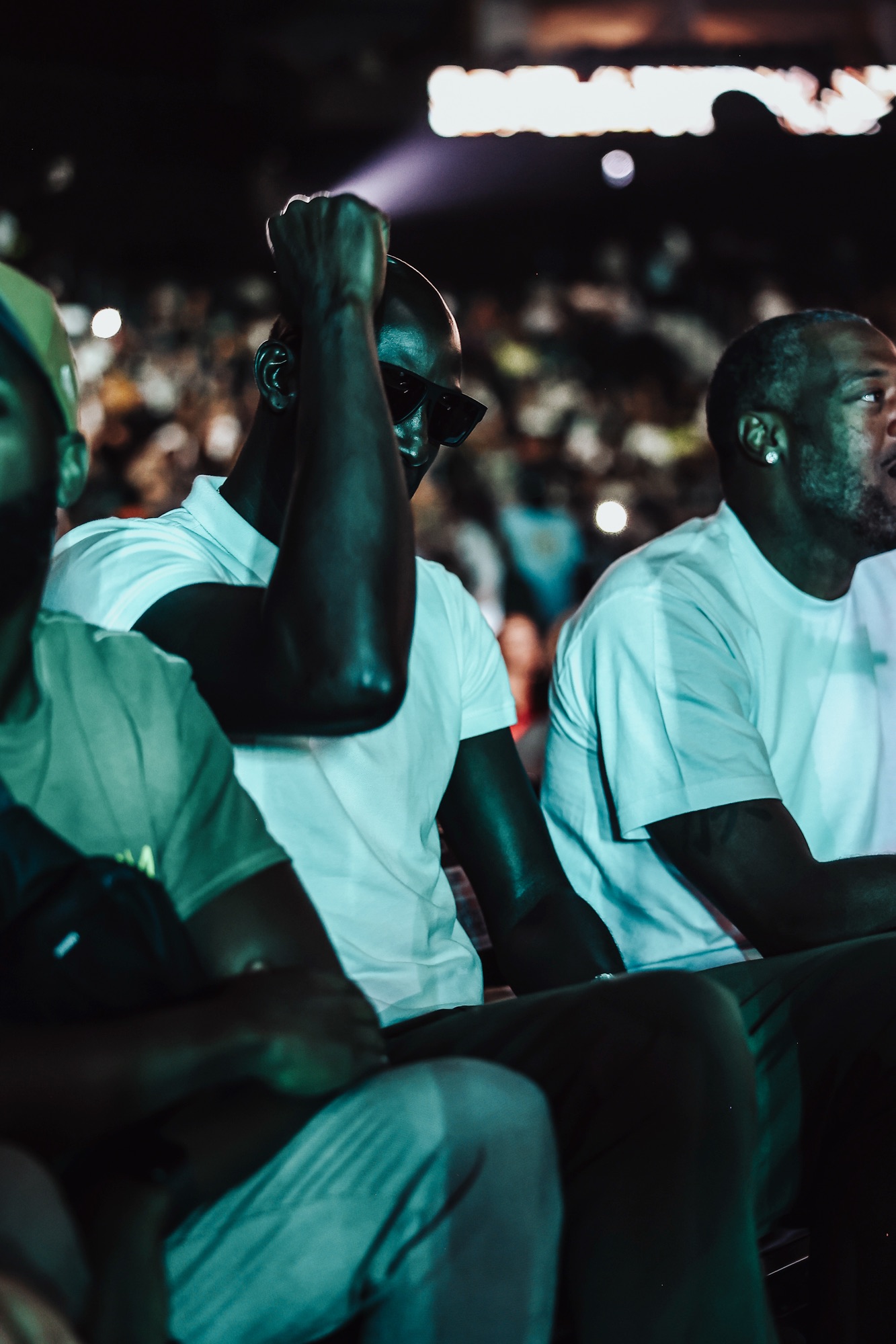 Spectators in white T-shirts watching from the stands under moody teal light