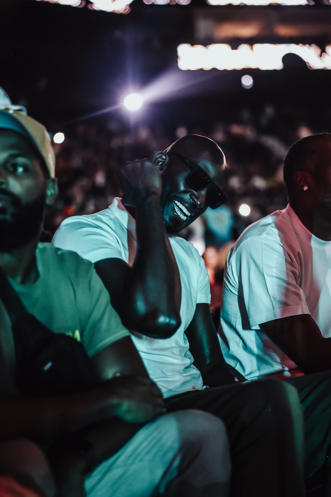 Grinning man in sunglasses seated in the crowd under arena spotlights