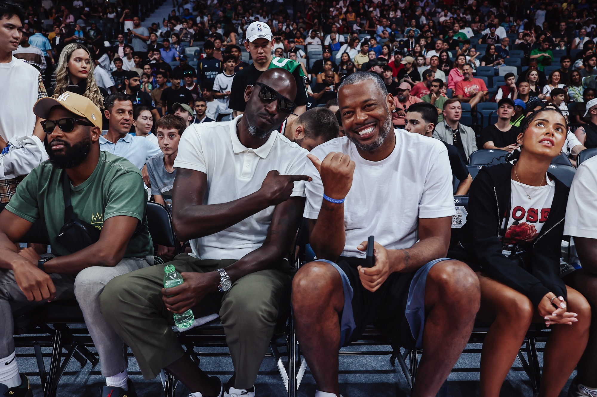 Two smiling men in white T-shirts posing courtside among fans