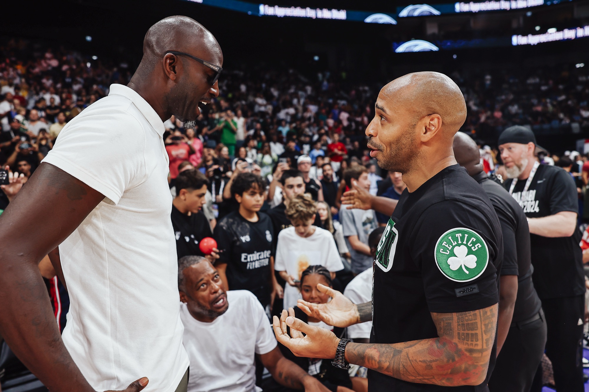 Man in a white polo chatting with a man in a Celtics T-shirt courtside