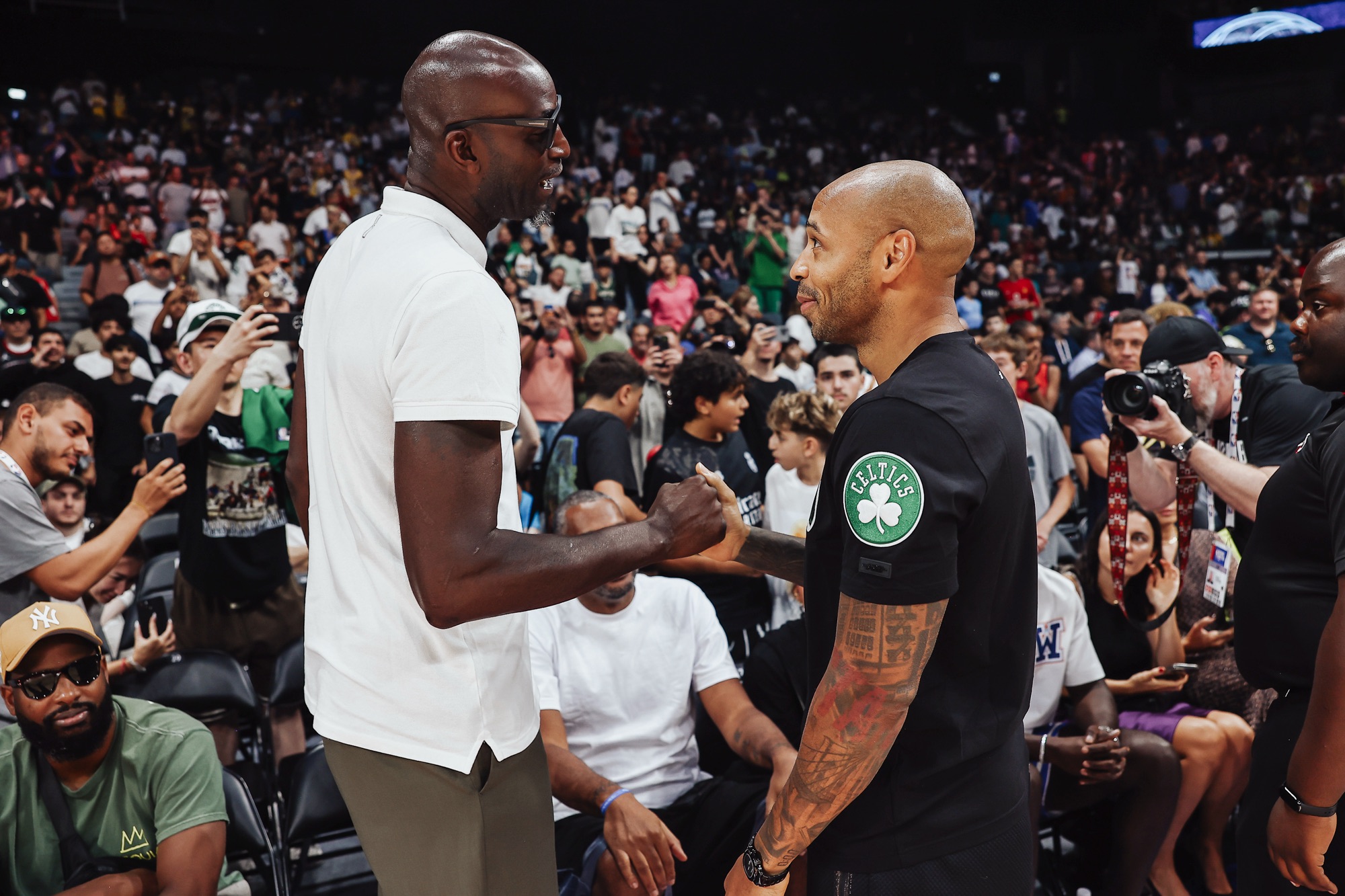 Two men shaking hands courtside as photographers and fans look on