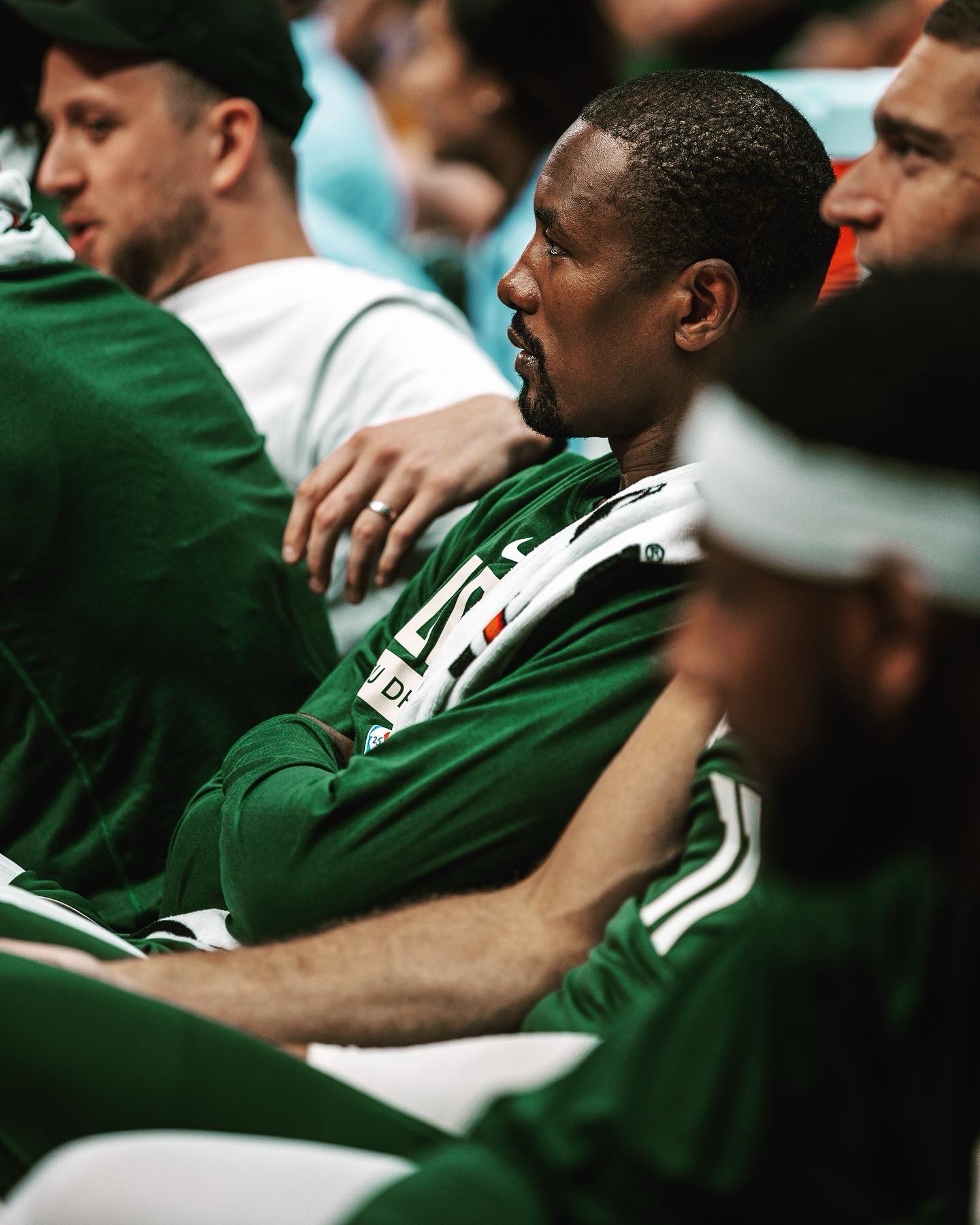 Player in a green Boston warm-up shirt watching intently from the bench
