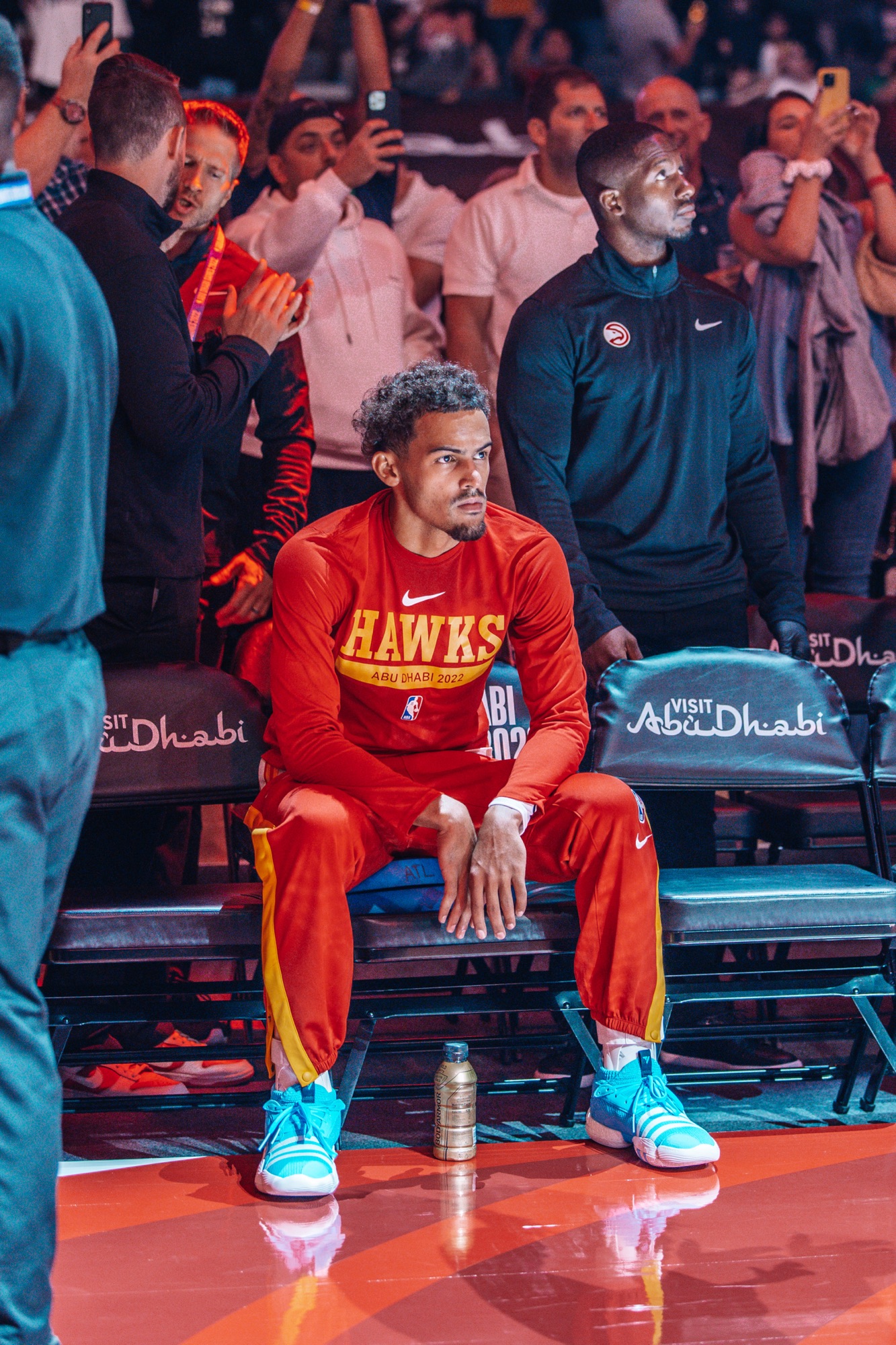 Player in a red Hawks warm-up suit seated courtside before tip-off