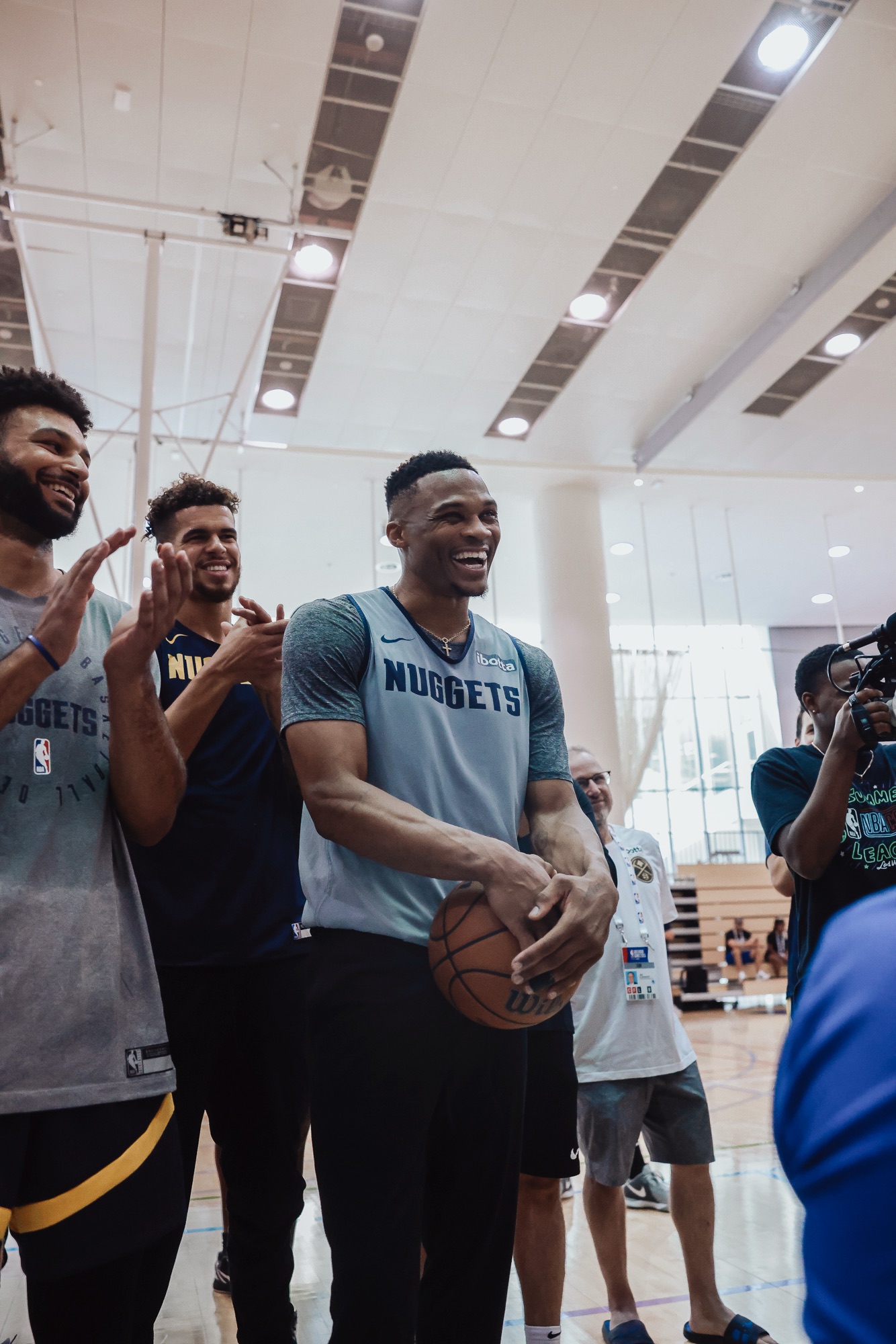 Laughing player in a Nuggets practice top holding a ball as teammates applaud