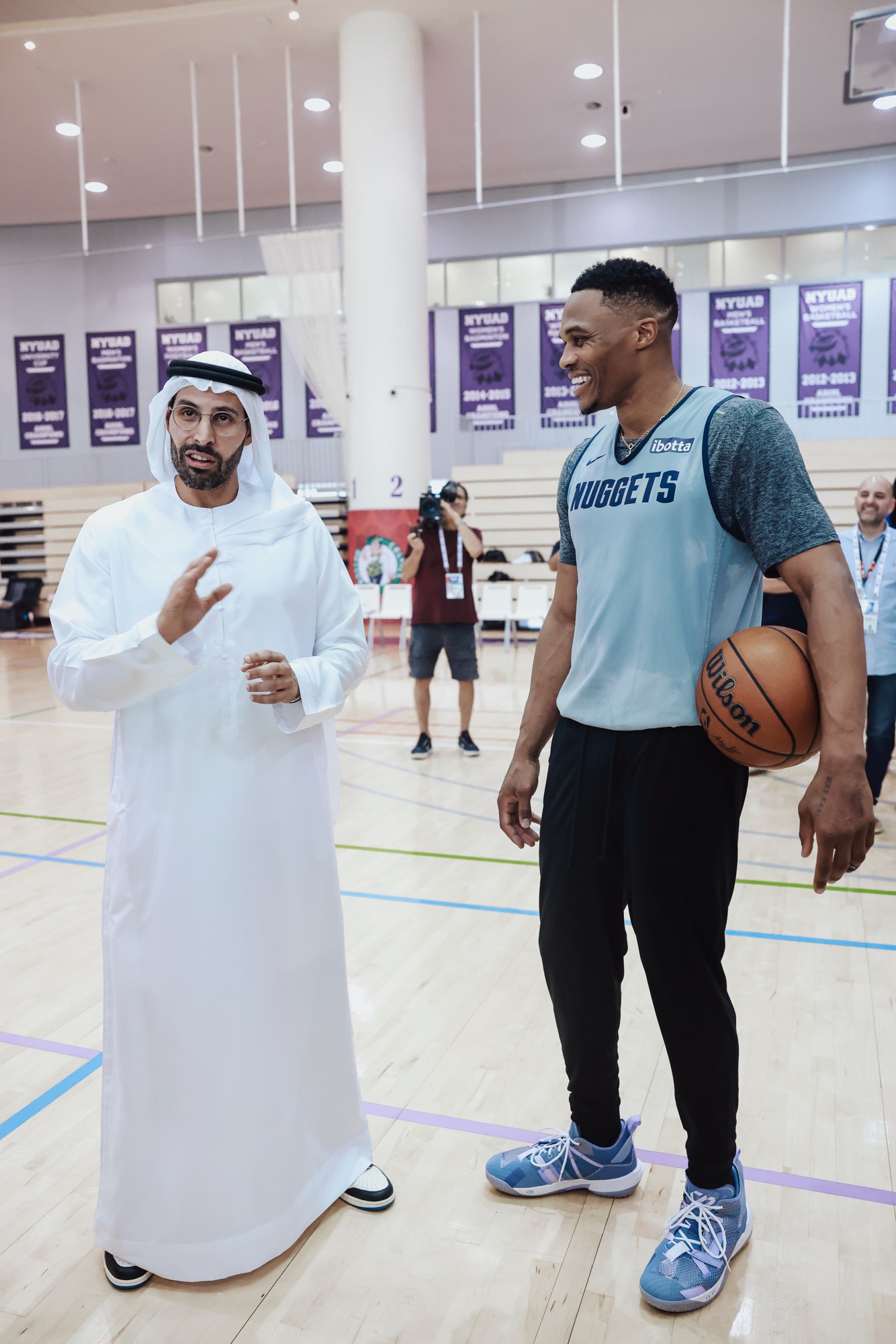 Man in a white kandura chatting with a smiling player in a Nuggets top
