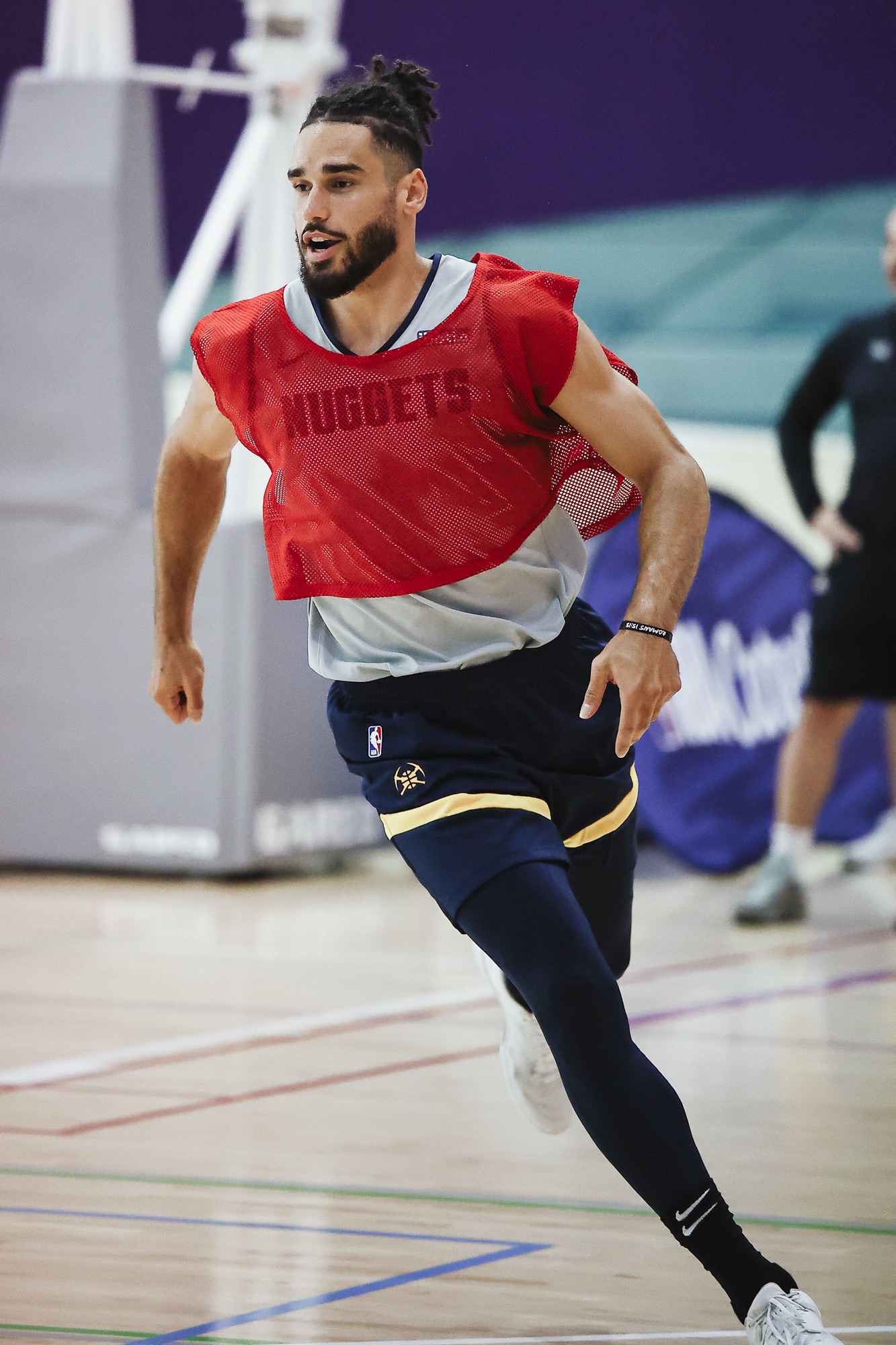 Player in a red Nuggets practice bib sprinting across the gym floor