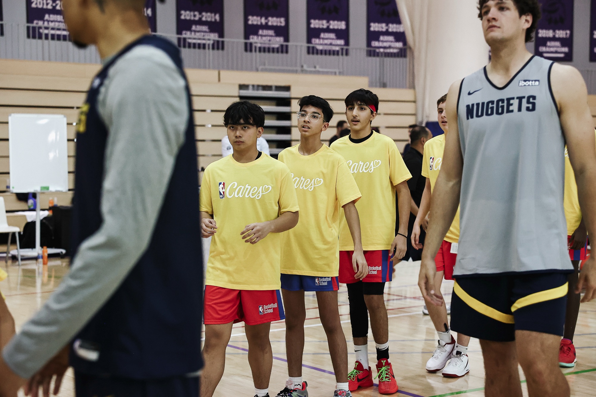 Young players in yellow NBA Cares shirts at a clinic alongside Nuggets players