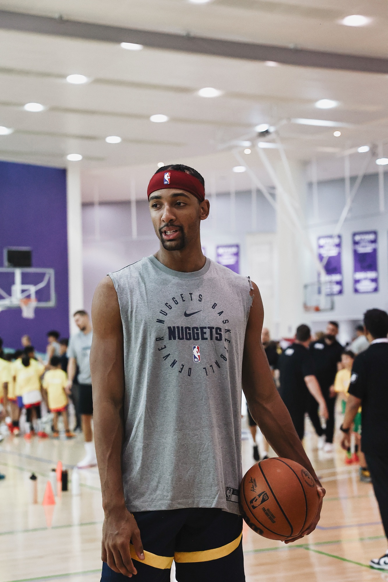 Player in a red headband and sleeveless Nuggets top holding a ball at a youth clinic