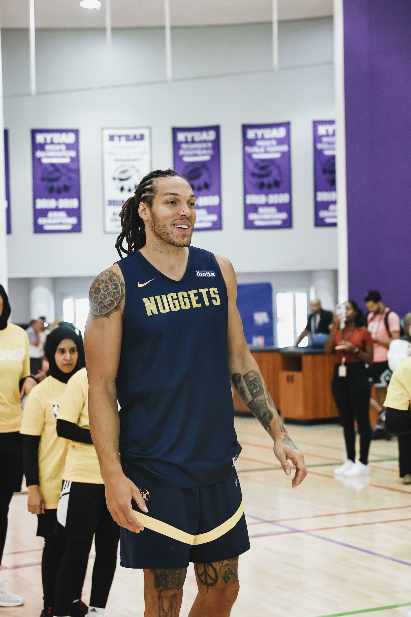 Smiling player in a navy Nuggets jersey at a youth clinic in the gym