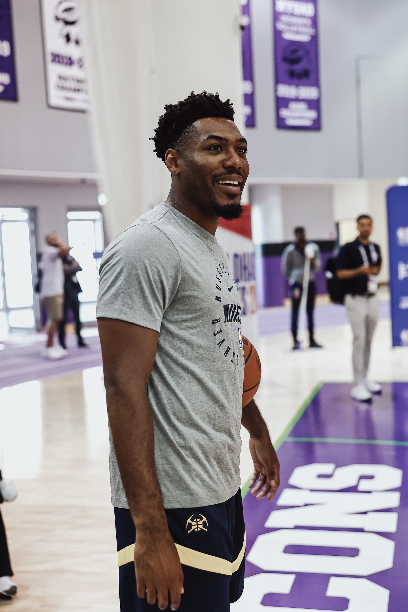 Player in a grey Nuggets T-shirt smiling on a purple-marked practice court
