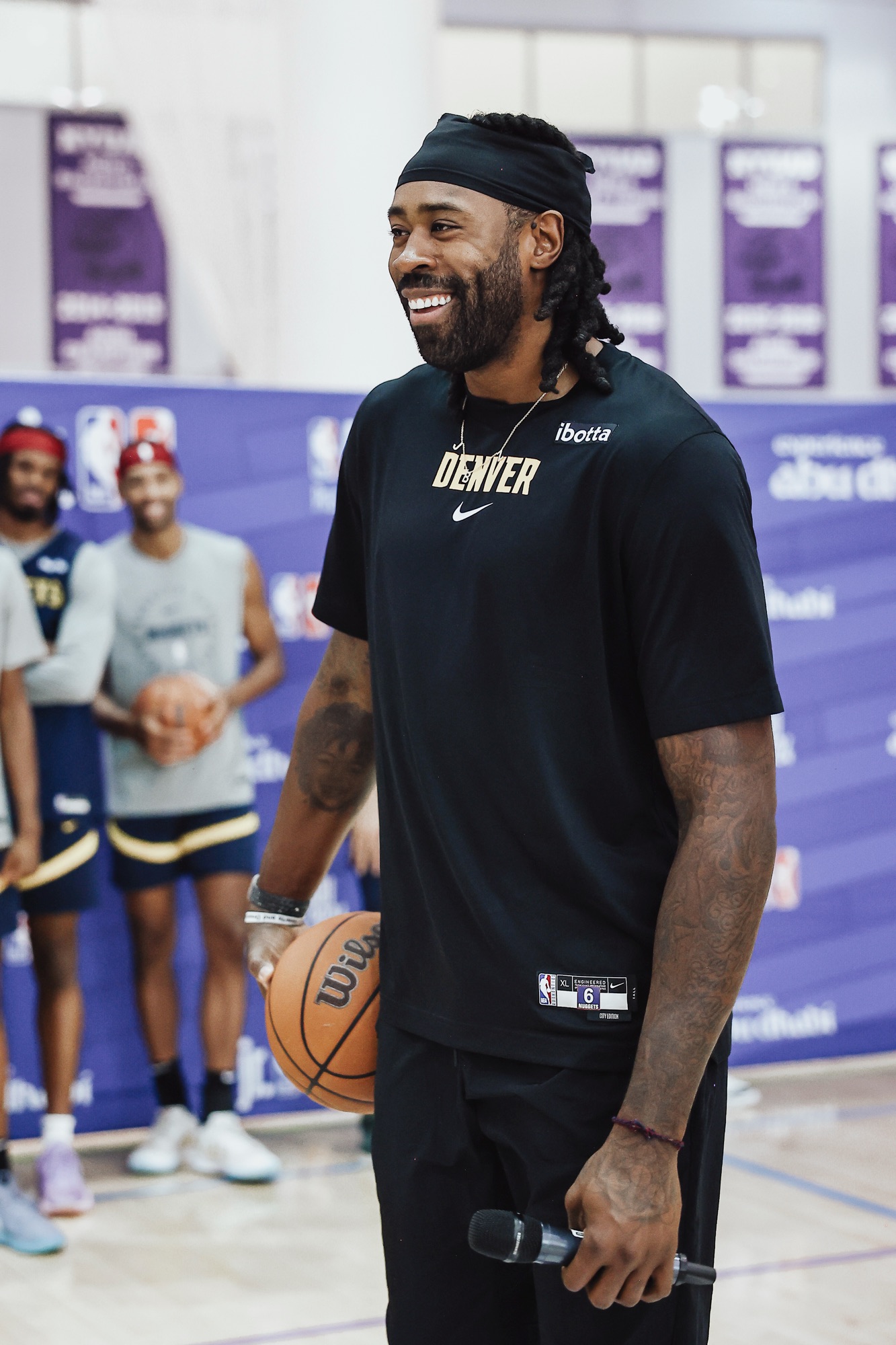 Smiling man in a black Denver T-shirt holding a ball and microphone at a clinic